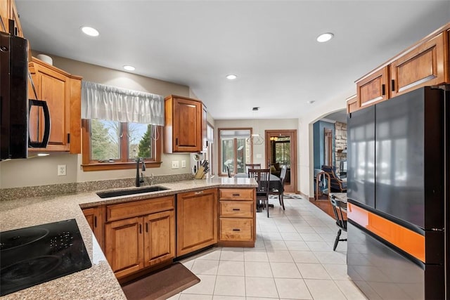 kitchen featuring brown cabinetry, arched walkways, a sink, and black appliances