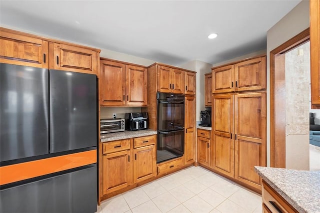 kitchen featuring light tile patterned flooring, a toaster, dobule oven black, freestanding refrigerator, and brown cabinets