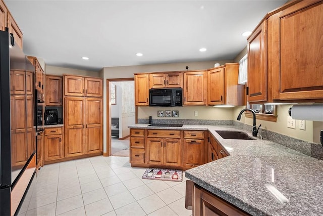 kitchen featuring brown cabinetry, stone counters, black appliances, a sink, and recessed lighting