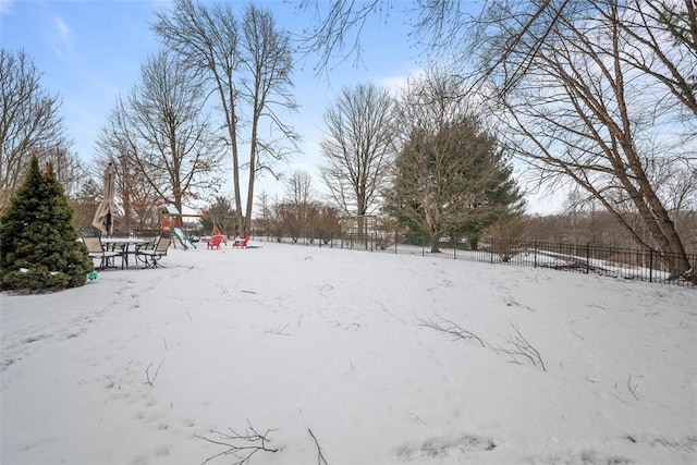 yard layered in snow featuring a playground and fence