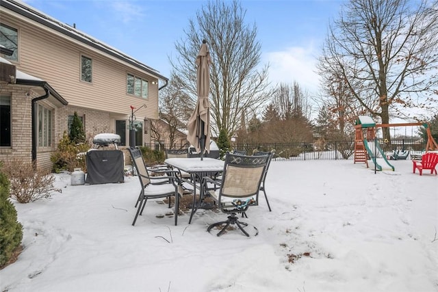 yard covered in snow with outdoor dining space, a playground, and fence