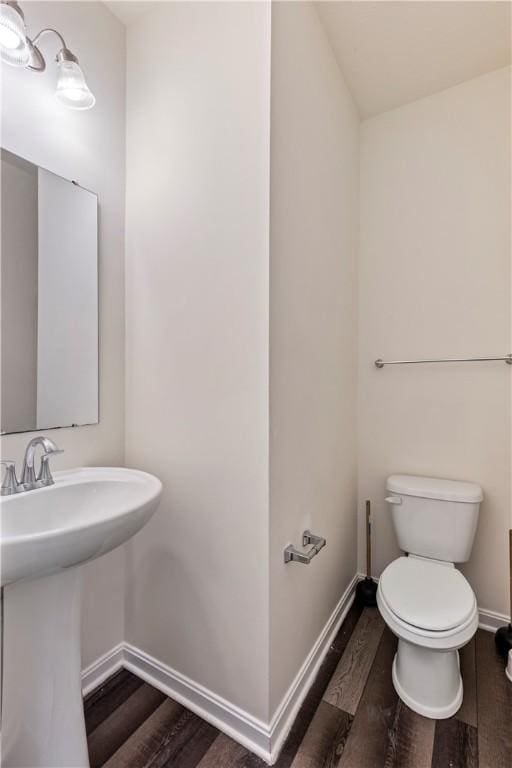 half bathroom featuring toilet, a sink, baseboards, and wood finished floors