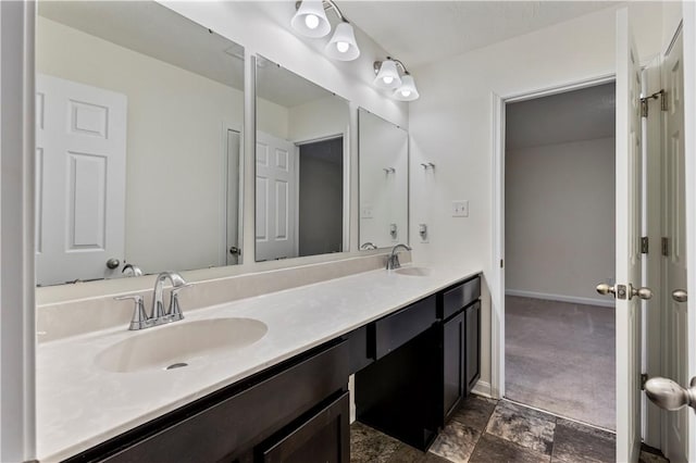 full bath featuring double vanity, stone finish floor, a sink, and baseboards