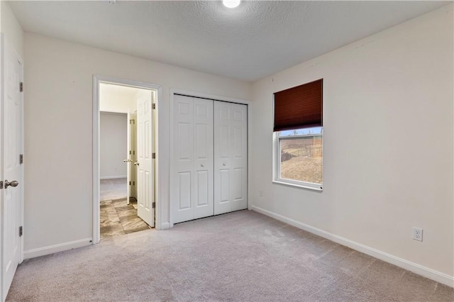 unfurnished bedroom with a textured ceiling, a closet, baseboards, and carpet flooring