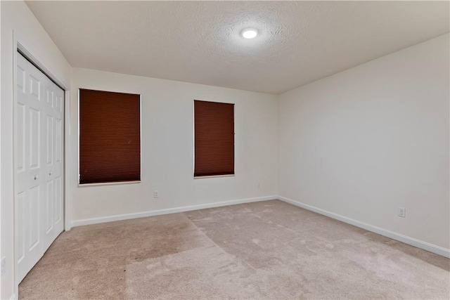 unfurnished bedroom featuring a closet, light colored carpet, a textured ceiling, and baseboards