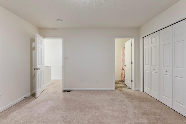 unfurnished bedroom featuring visible vents, baseboards, light colored carpet, ensuite bath, and a closet