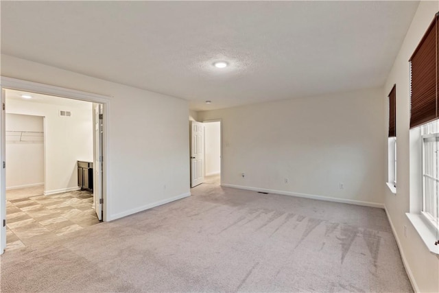 unfurnished room with baseboards, visible vents, a textured ceiling, and light colored carpet