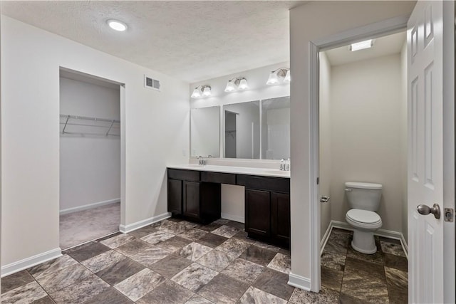 bathroom with a walk in closet, double vanity, visible vents, a textured ceiling, and baseboards