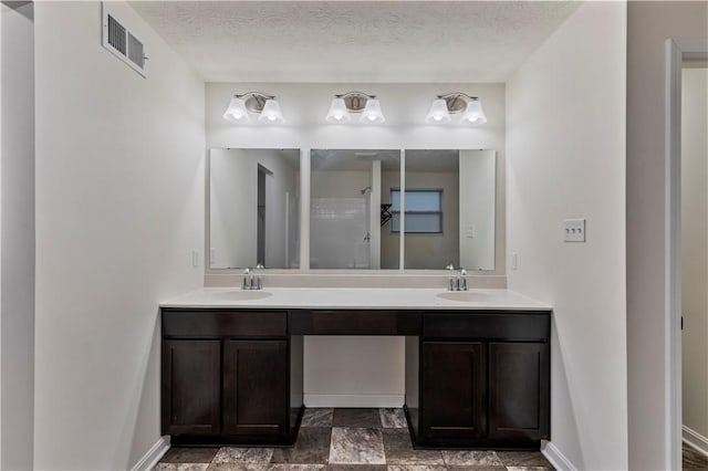 full bathroom with a textured ceiling, double vanity, a sink, and visible vents