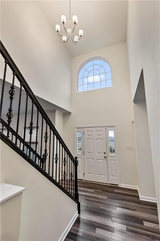 foyer entrance featuring a notable chandelier, wood finished floors, a towering ceiling, baseboards, and stairs