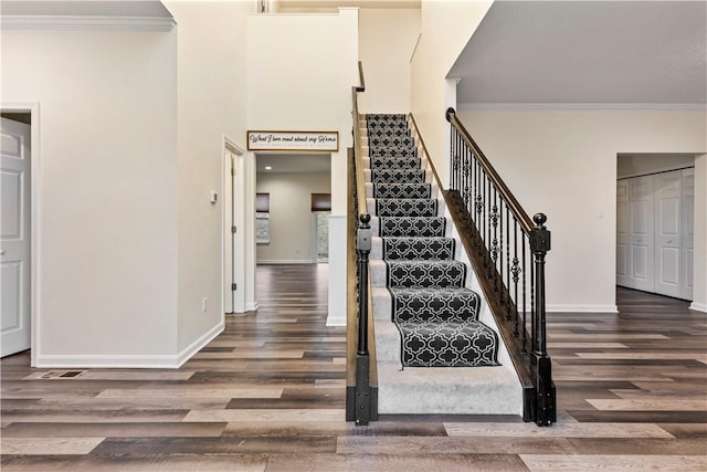 stairs with a towering ceiling, baseboards, crown molding, and wood finished floors