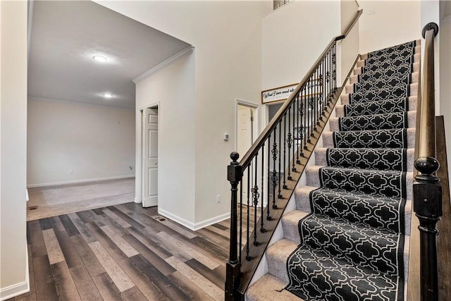 stairs with a towering ceiling, baseboards, wood finished floors, and ornamental molding