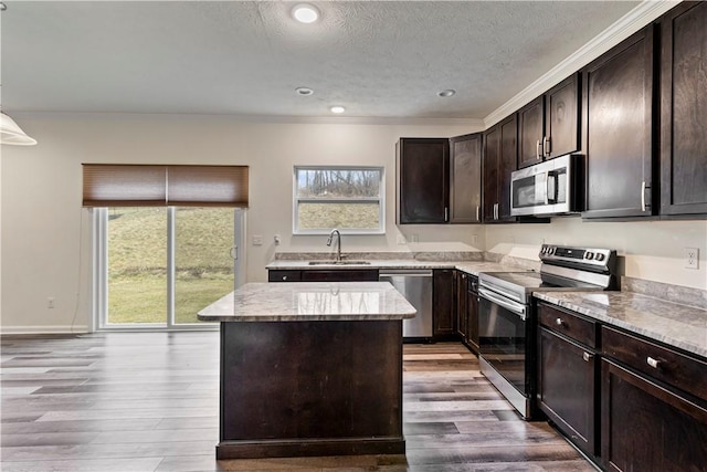 kitchen featuring stainless steel appliances, wood finished floors, a kitchen island, and a sink