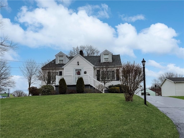 cape cod house featuring concrete driveway, a shingled roof, a chimney, and a front yard