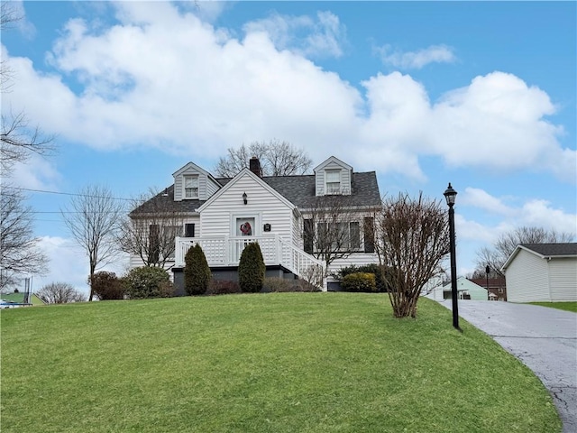 cape cod-style house featuring a shingled roof, a front yard, concrete driveway, and a chimney