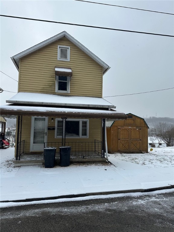 snow covered rear of property featuring covered porch