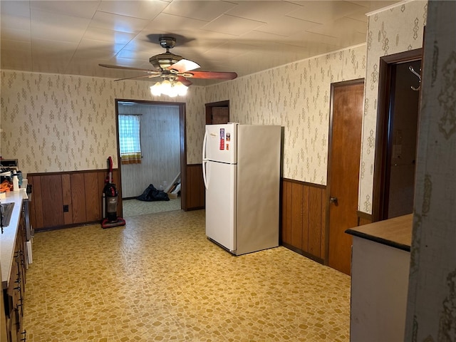 kitchen with a wainscoted wall, light floors, a ceiling fan, freestanding refrigerator, and wallpapered walls