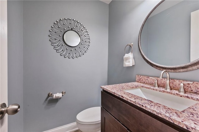 half bathroom with toilet, baseboards, and vanity