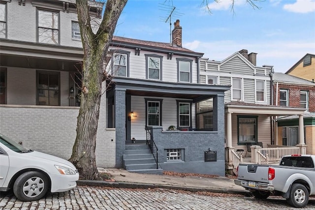 multi unit property featuring covered porch, brick siding, and a chimney