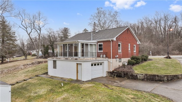 exterior space featuring brick siding, a lawn, an attached garage, a sunroom, and driveway