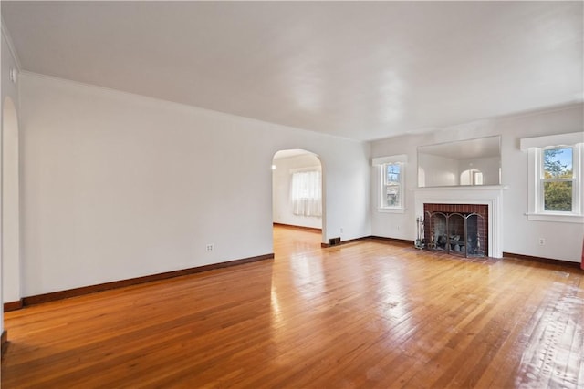 unfurnished living room featuring arched walkways, hardwood / wood-style floors, a fireplace, and baseboards