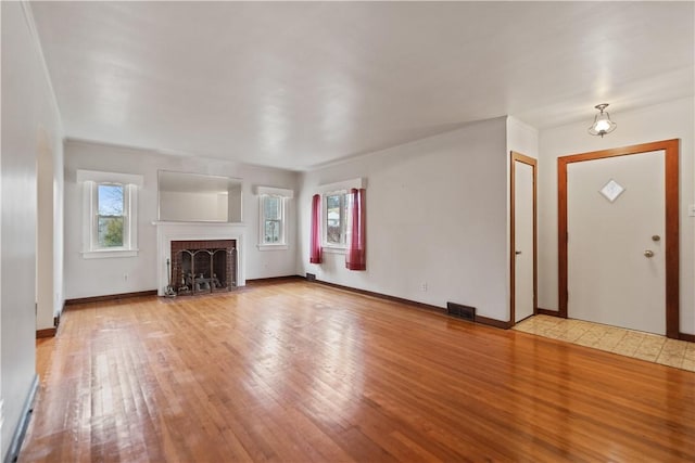 unfurnished living room featuring hardwood / wood-style flooring, a brick fireplace, visible vents, and baseboards