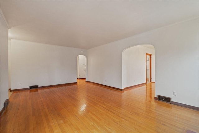 spare room featuring arched walkways, light wood-type flooring, visible vents, and baseboards