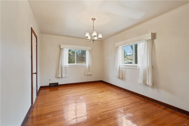 spare room featuring a chandelier, light wood-type flooring, baseboards, and crown molding