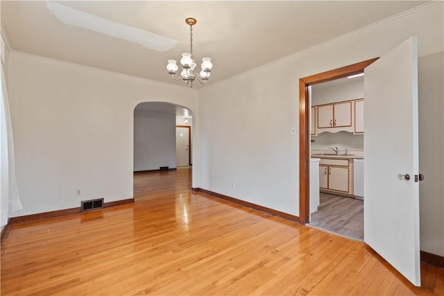 spare room featuring arched walkways, visible vents, light wood finished floors, an inviting chandelier, and crown molding