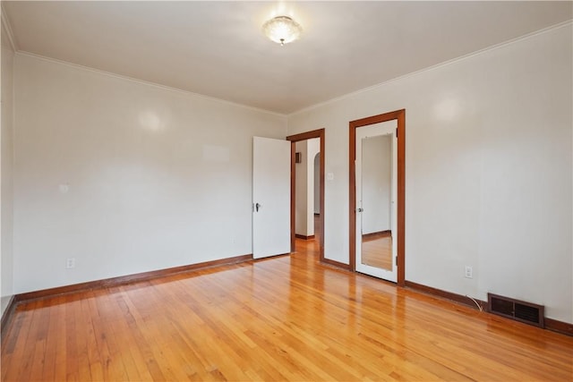 empty room featuring ornamental molding, light wood finished floors, visible vents, and baseboards