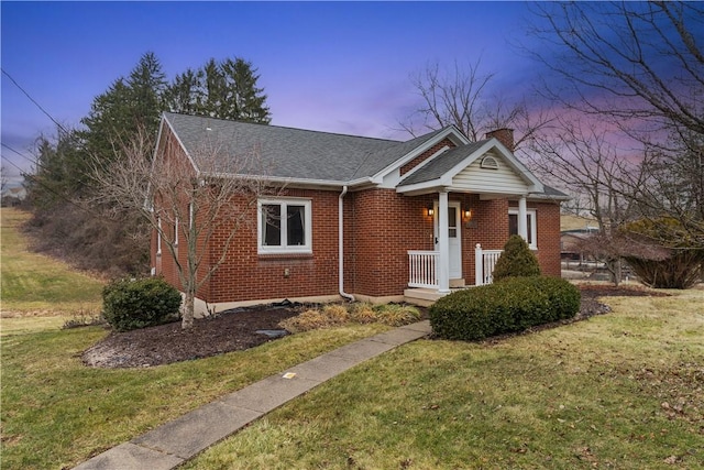 view of front of property featuring a shingled roof, a chimney, a lawn, and brick siding