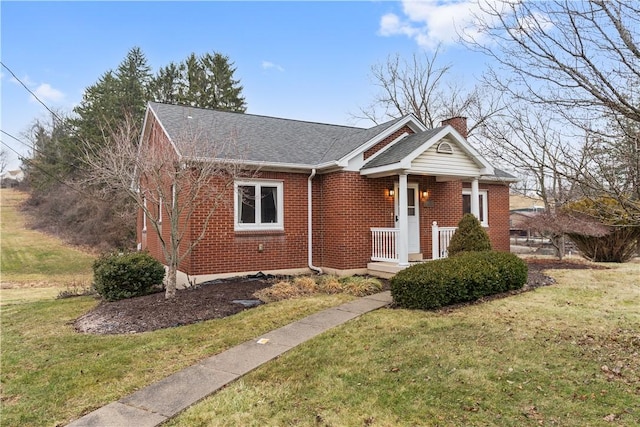 view of front of house with roof with shingles, a chimney, a front lawn, and brick siding