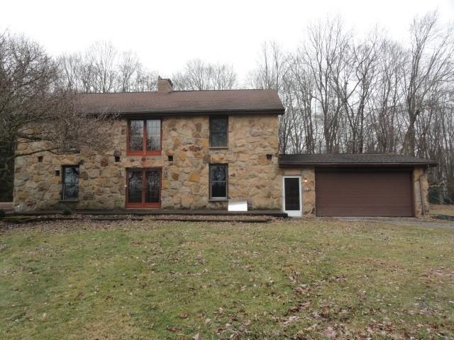 back of house with a garage, a yard, a chimney, and stone siding