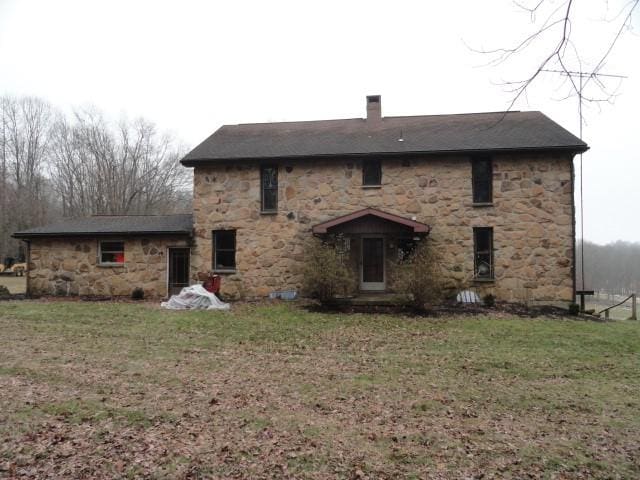 rear view of house featuring stone siding, a lawn, and a chimney