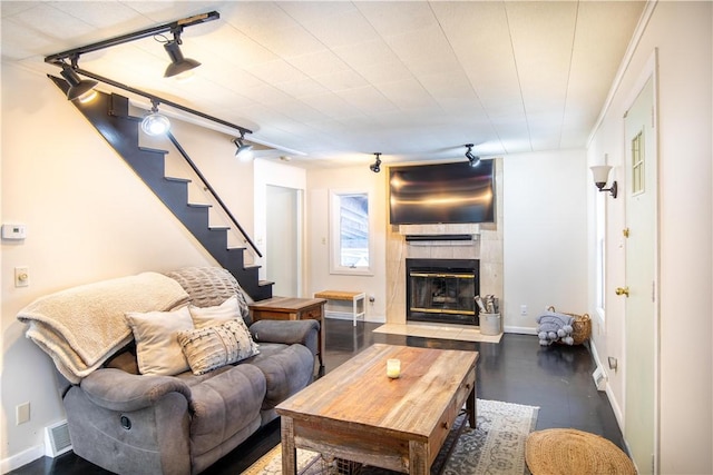 living room featuring stairs, a tiled fireplace, rail lighting, and baseboards