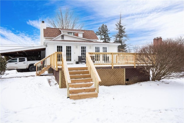 snow covered rear of property with stairs, french doors, a wooden deck, a carport, and a chimney