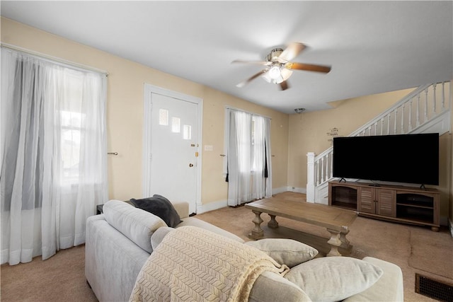 carpeted living area featuring stairway, baseboards, visible vents, and a ceiling fan