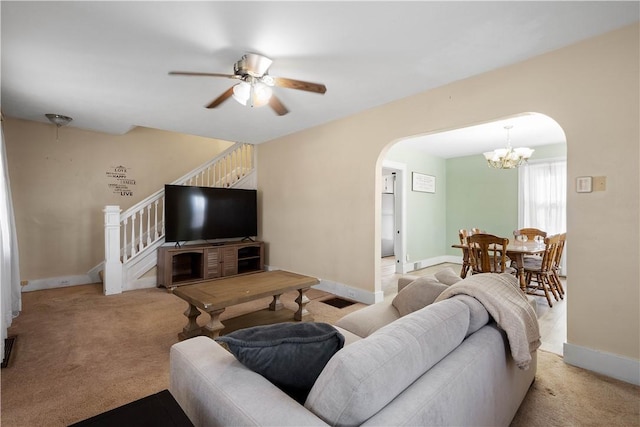 living area featuring carpet floors, arched walkways, stairway, baseboards, and ceiling fan with notable chandelier