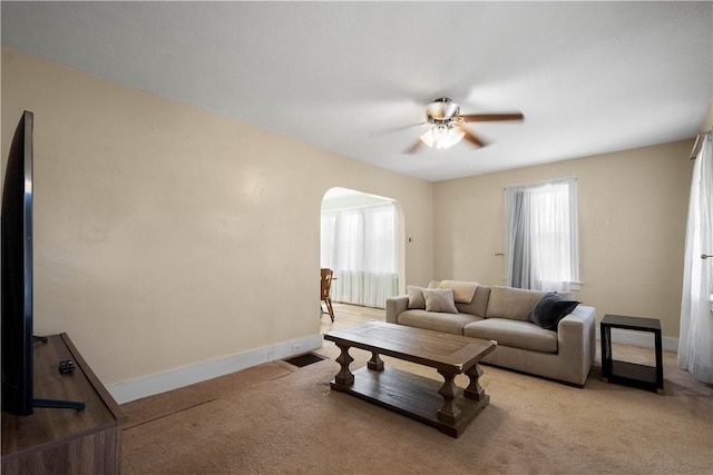 living area featuring light carpet, baseboards, visible vents, arched walkways, and a ceiling fan