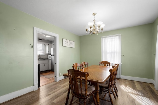 dining area featuring baseboards, light wood-style floors, a notable chandelier, and a healthy amount of sunlight