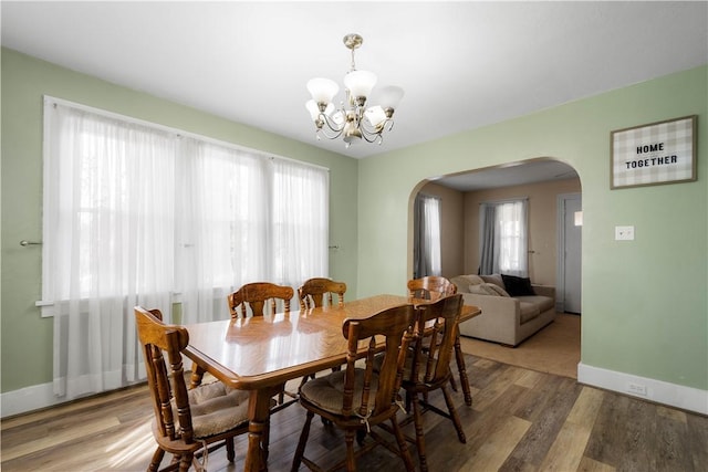 dining room featuring light wood-type flooring, arched walkways, baseboards, and an inviting chandelier