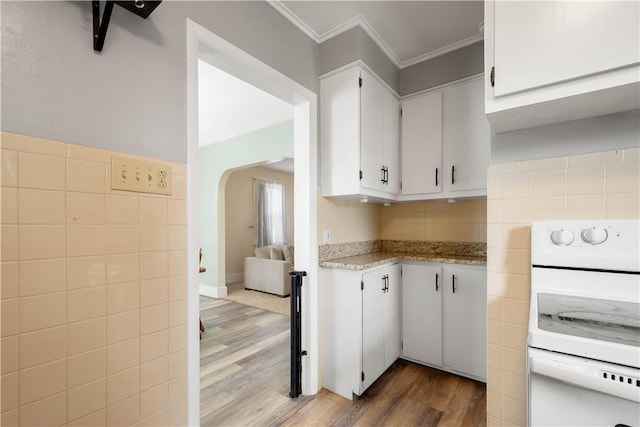 kitchen with electric range, arched walkways, white cabinets, crown molding, and light wood-style floors