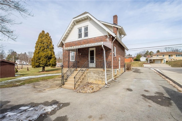 view of property exterior featuring an outbuilding, covered porch, brick siding, a detached garage, and a chimney