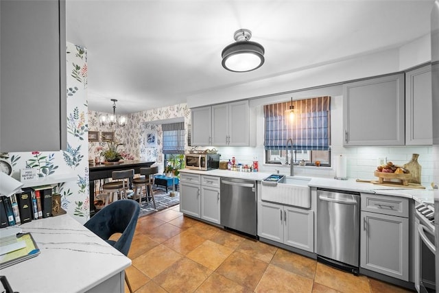 kitchen featuring a notable chandelier, stainless steel appliances, gray cabinets, a sink, and wallpapered walls