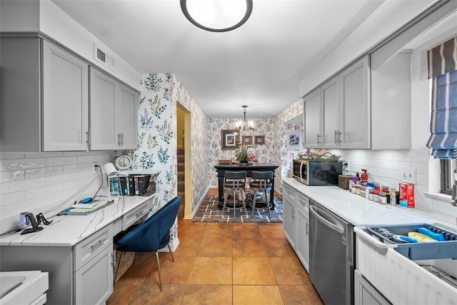 kitchen featuring wallpapered walls, appliances with stainless steel finishes, an inviting chandelier, gray cabinets, and light tile patterned flooring