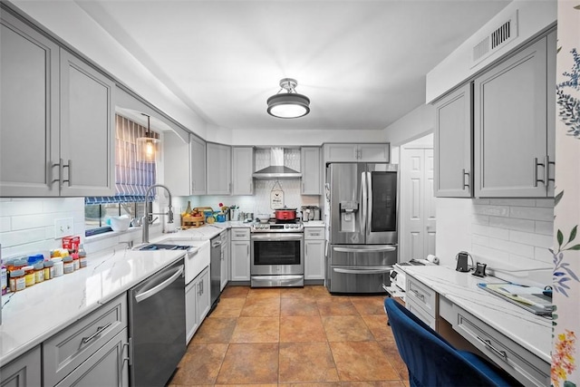 kitchen featuring appliances with stainless steel finishes, gray cabinets, light stone counters, and wall chimney exhaust hood