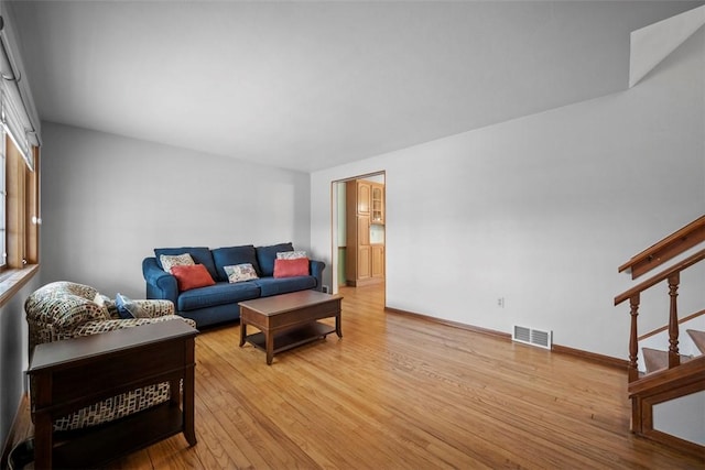 living room with stairs, wood finished floors, visible vents, and baseboards