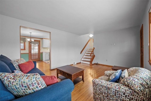 living area with a notable chandelier, light wood-style flooring, baseboards, and stairs