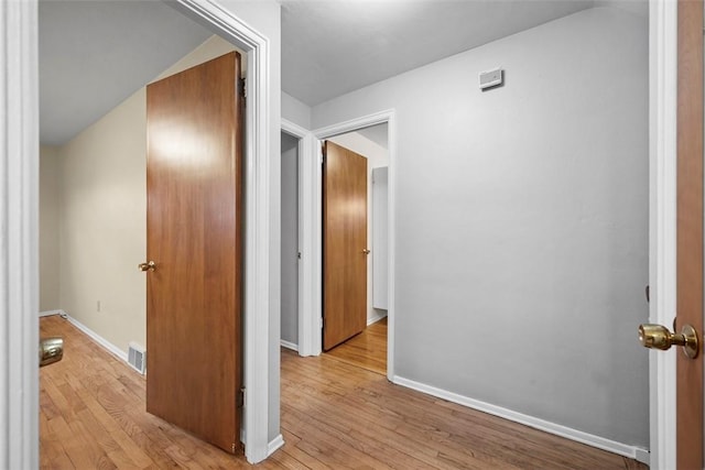 corridor with light wood-type flooring, visible vents, and baseboards