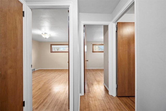 corridor with light wood-style floors, visible vents, and baseboards